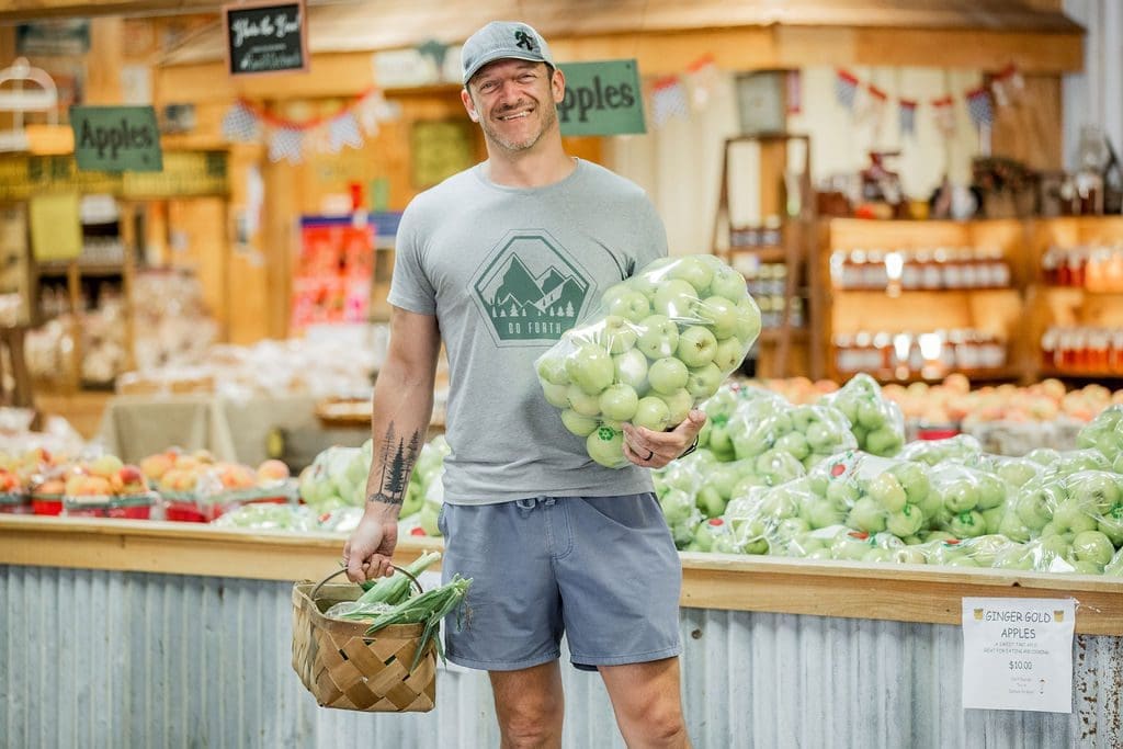 a man holding a bag of fresh apples and corn